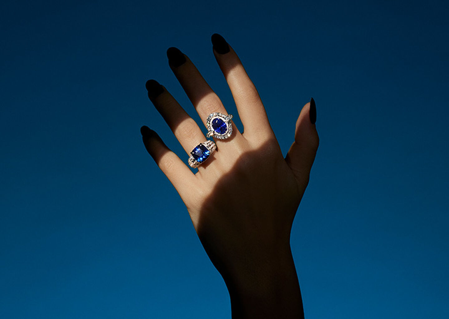 A woman's hand wearing sapphire and diamonds rings from the Maison Birks high jewellery collection on a blue background